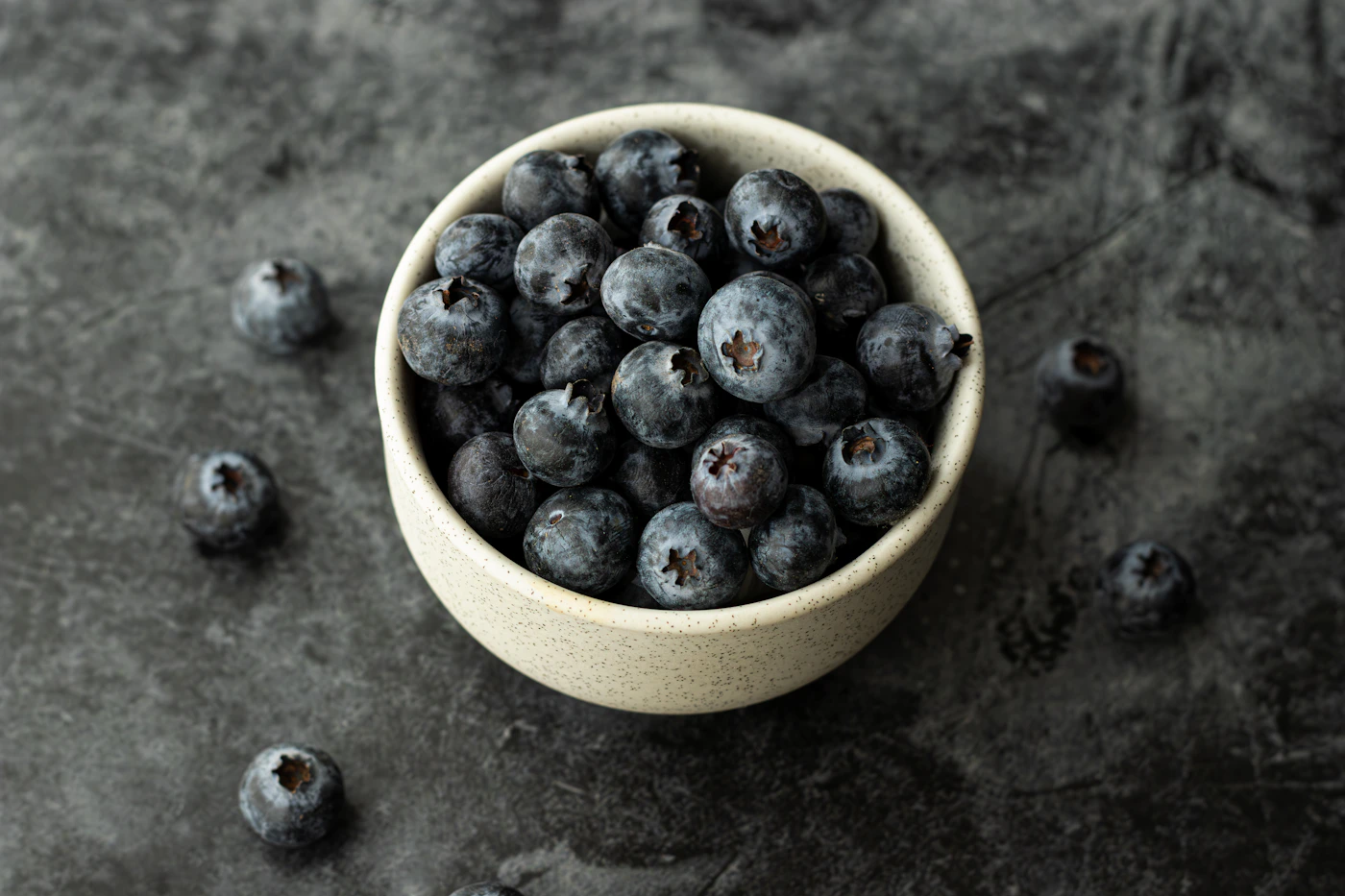 Fresh blueberries in a white ceramic bowl on a dark textured table.